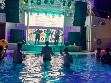 A band playing on a stage. In front of the stage is a pool with persons, one of them me. Behind the stage is a screen with a conference slide announcing the resource track. The slide has my headshot.